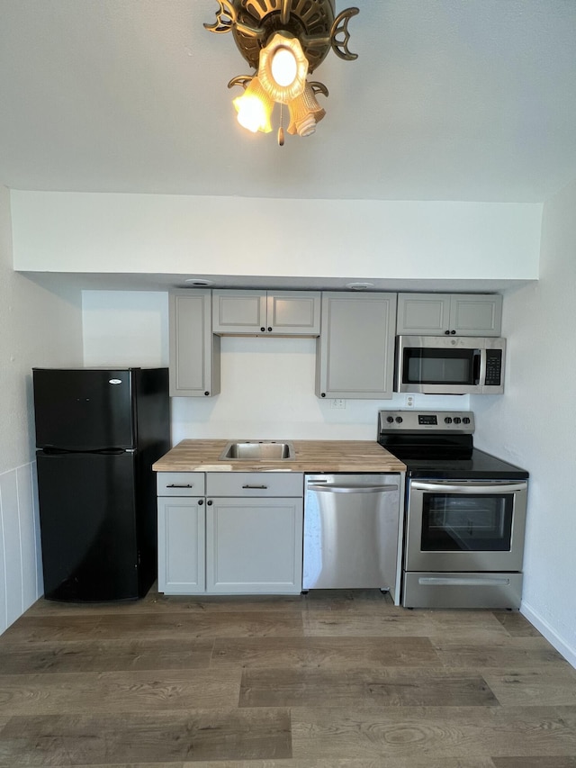 kitchen featuring dark hardwood / wood-style flooring, stainless steel appliances, sink, gray cabinets, and butcher block countertops