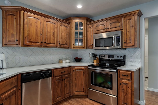 kitchen featuring light stone countertops, light wood-type flooring, appliances with stainless steel finishes, and tasteful backsplash