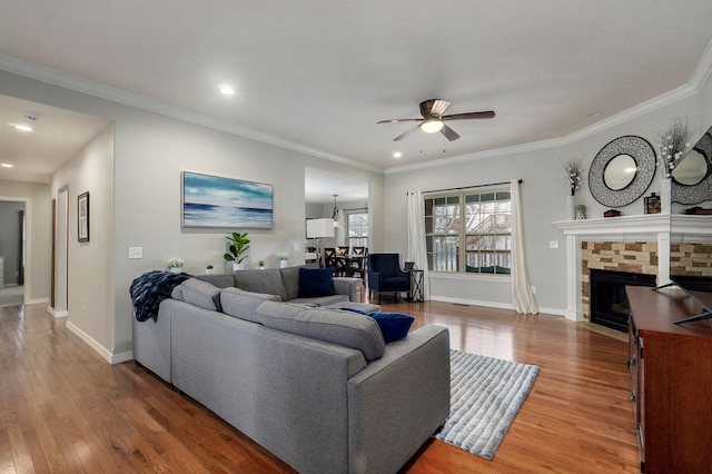 living room with hardwood / wood-style floors, ceiling fan, a stone fireplace, and ornamental molding