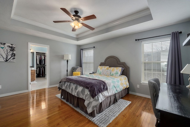 bedroom featuring ceiling fan, a raised ceiling, a spacious closet, and ornamental molding