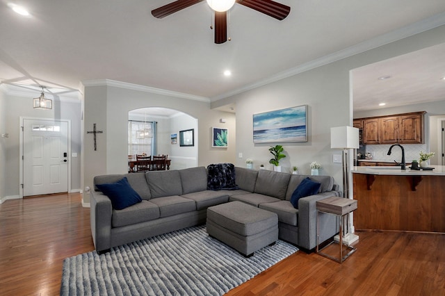 living room featuring ceiling fan with notable chandelier, dark hardwood / wood-style flooring, crown molding, and sink