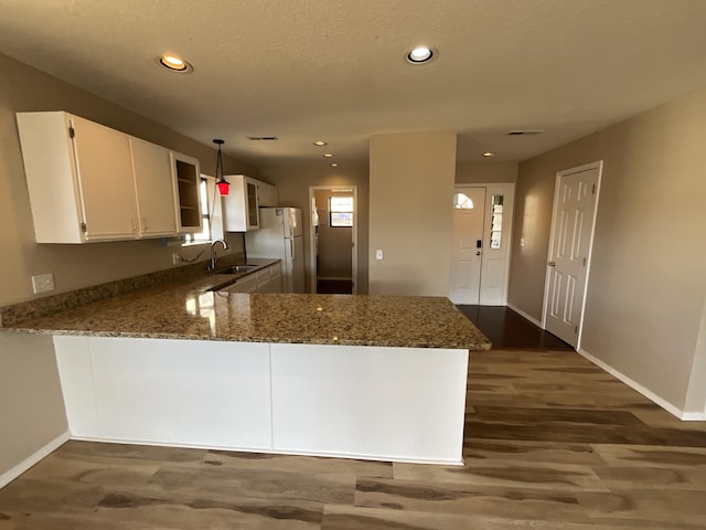 kitchen with sink, dark wood-type flooring, kitchen peninsula, white fridge, and white cabinets