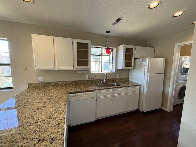 kitchen with white appliances, white cabinets, sink, hanging light fixtures, and stacked washer / drying machine