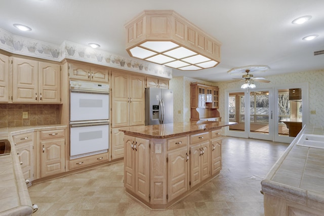 kitchen with a center island, white double oven, light brown cabinets, ceiling fan, and stainless steel fridge with ice dispenser