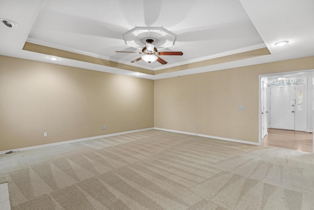 carpeted spare room featuring a raised ceiling, ceiling fan, and ornamental molding