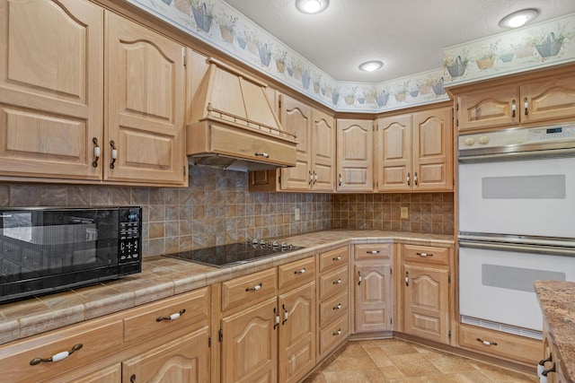 kitchen featuring premium range hood, tasteful backsplash, tile counters, and black appliances