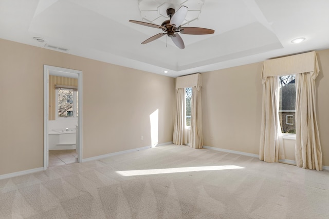 spare room featuring light colored carpet, a raised ceiling, and ceiling fan