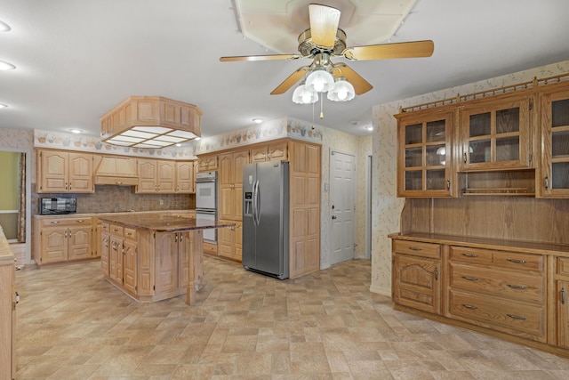 kitchen with stainless steel fridge, custom range hood, double oven, ceiling fan, and a kitchen island