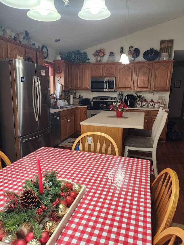 kitchen featuring sink, stainless steel appliances, decorative light fixtures, vaulted ceiling, and a kitchen island