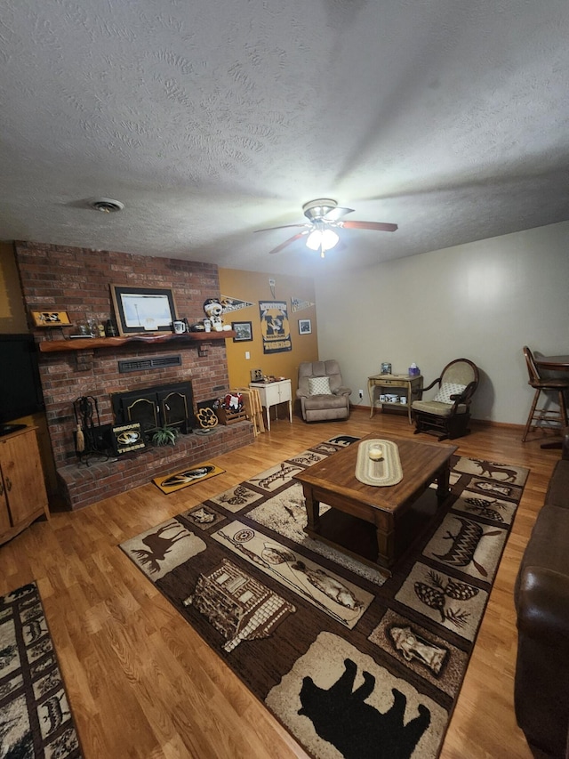 living room featuring hardwood / wood-style flooring, ceiling fan, a wood stove, and a textured ceiling