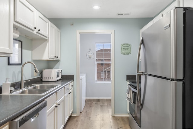 kitchen with light wood-type flooring, stainless steel appliances, sink, white cabinets, and washing machine and dryer