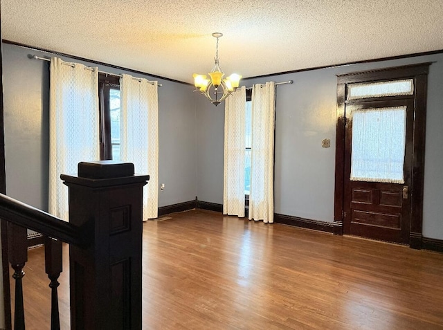 unfurnished room featuring baseboards, ornamental molding, an inviting chandelier, wood finished floors, and a textured ceiling