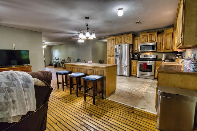 kitchen featuring a breakfast bar, sink, appliances with stainless steel finishes, decorative light fixtures, and a kitchen island