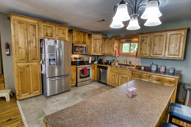 kitchen with a kitchen bar, stainless steel appliances, sink, pendant lighting, and a chandelier