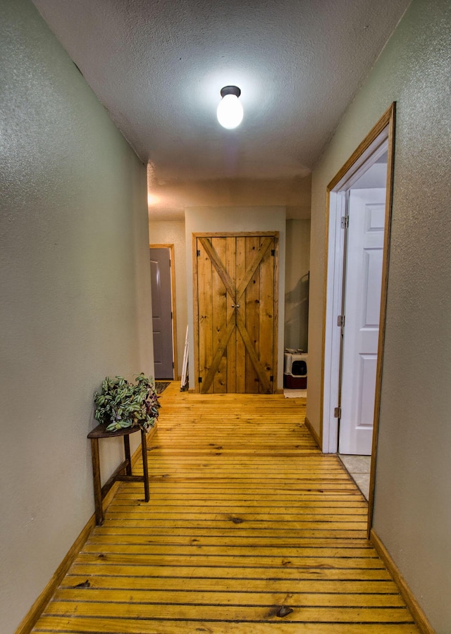 corridor with light wood-type flooring and a textured ceiling