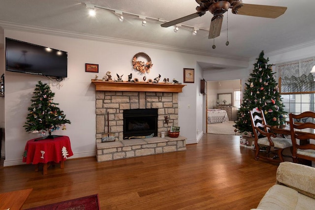 living room with wood-type flooring, a stone fireplace, ceiling fan, and crown molding