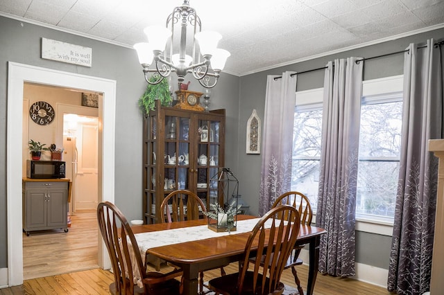 dining area with light wood-type flooring, an inviting chandelier, a wealth of natural light, and crown molding