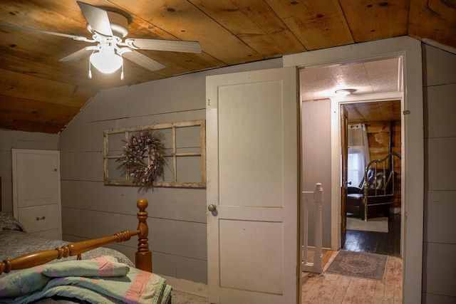 bedroom with ceiling fan, wooden walls, wooden ceiling, hardwood / wood-style floors, and lofted ceiling