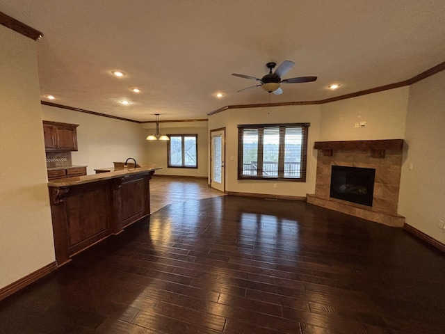 unfurnished living room with ceiling fan, dark hardwood / wood-style floors, a stone fireplace, and crown molding