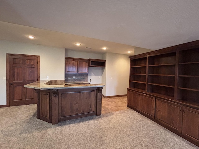 kitchen featuring dark brown cabinets, light colored carpet, and a kitchen island with sink