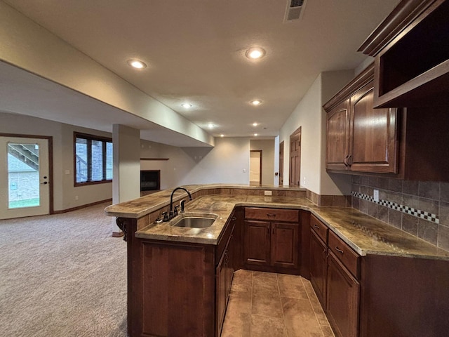 kitchen with sink, backsplash, kitchen peninsula, light colored carpet, and dark brown cabinets