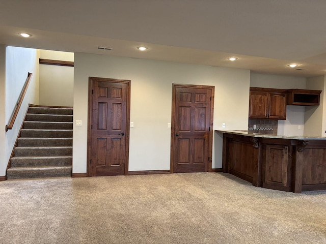 kitchen featuring dark brown cabinets, light colored carpet, tasteful backsplash, and a kitchen breakfast bar