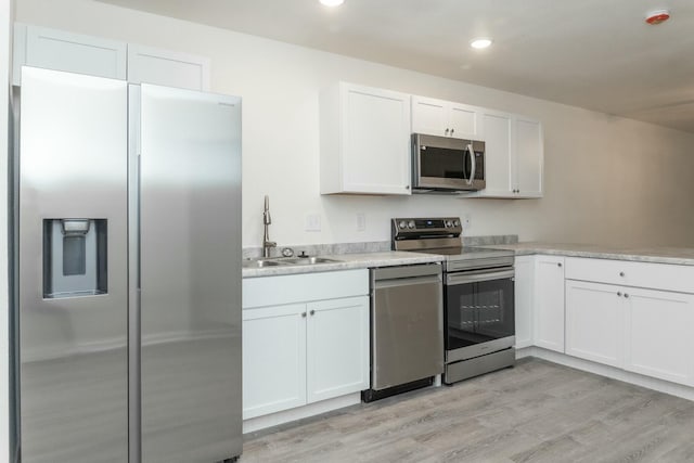 kitchen featuring stainless steel appliances, white cabinetry, light hardwood / wood-style floors, and sink