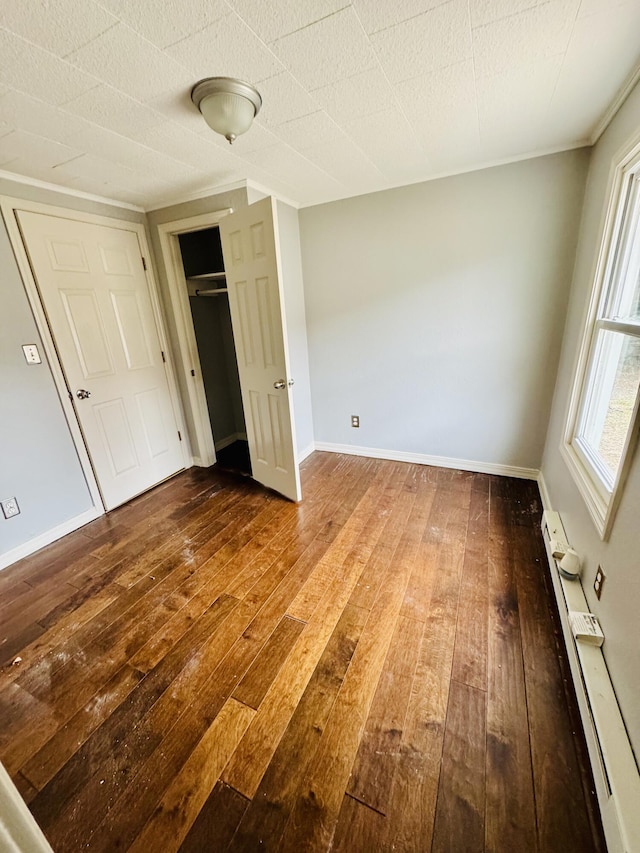 unfurnished bedroom featuring hardwood / wood-style flooring and a baseboard heating unit