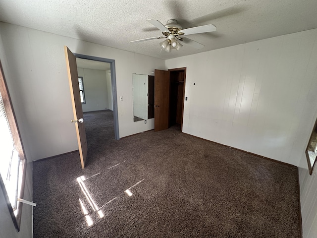 unfurnished bedroom featuring a textured ceiling, dark carpet, and ceiling fan