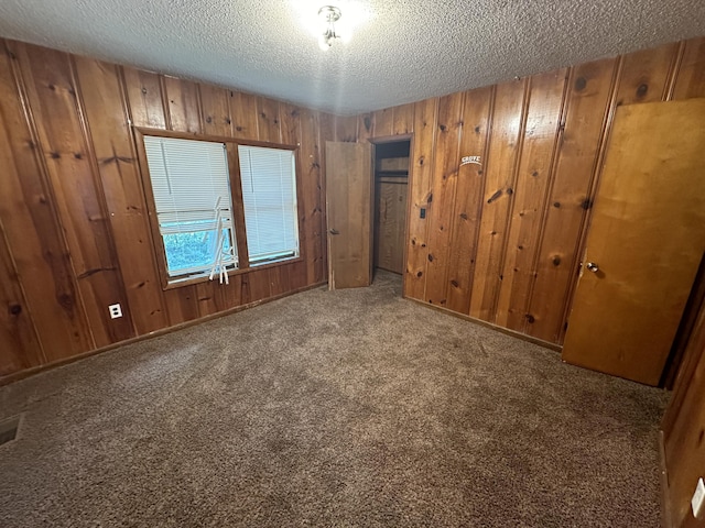 carpeted empty room featuring a textured ceiling and wood walls