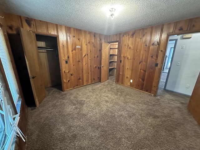 unfurnished bedroom with carpet flooring, a textured ceiling, a closet, and wooden walls