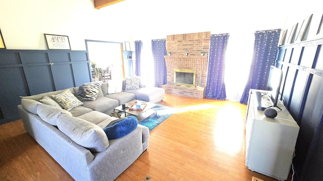 living room featuring beamed ceiling, wood-type flooring, and a brick fireplace