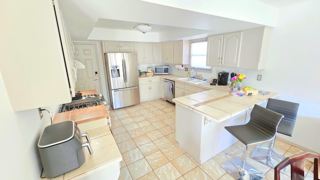 kitchen featuring sink, a breakfast bar area, light tile patterned floors, kitchen peninsula, and stainless steel appliances