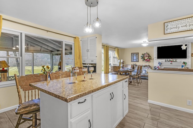 kitchen featuring light stone countertops, a center island, white cabinetry, hanging light fixtures, and a breakfast bar area