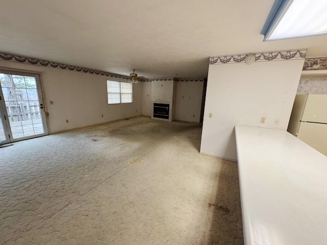 interior space with a tile fireplace, ceiling fan, and light colored carpet