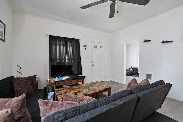 living room featuring ceiling fan, crown molding, wood-type flooring, and a textured ceiling