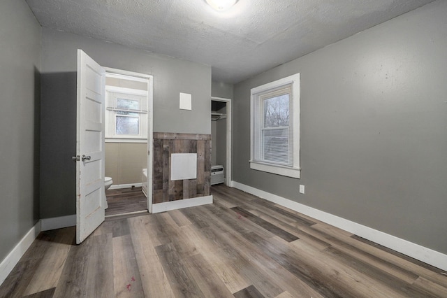 unfurnished bedroom featuring baseboard heating, a textured ceiling, and dark hardwood / wood-style floors