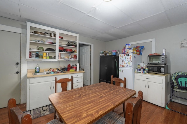 kitchen featuring a paneled ceiling, black fridge, sink, dark hardwood / wood-style floors, and white cabinetry