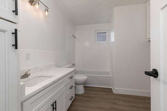 full bathroom with hardwood / wood-style floors, vanity, tiled shower / bath combo, toilet, and a textured ceiling