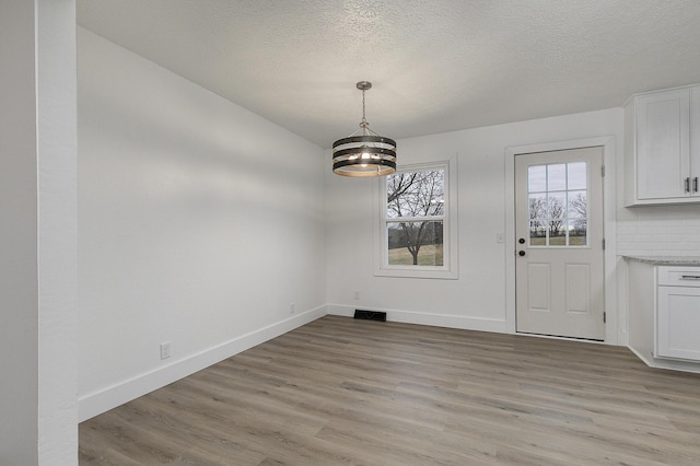 unfurnished dining area with a textured ceiling, light hardwood / wood-style flooring, and an inviting chandelier