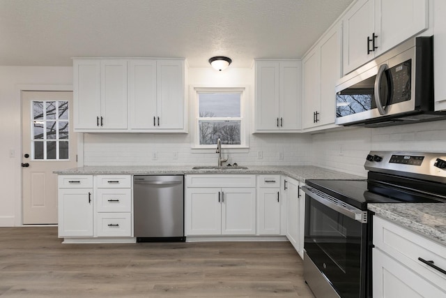 kitchen with light stone countertops, light wood-type flooring, stainless steel appliances, sink, and white cabinetry