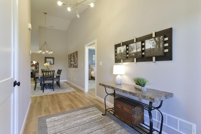 corridor with hardwood / wood-style floors, a notable chandelier, and high vaulted ceiling