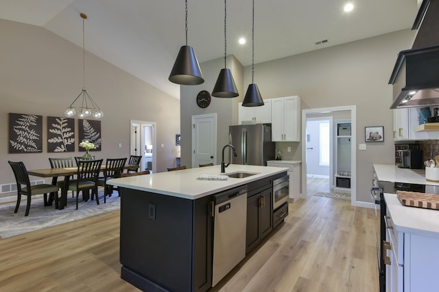 kitchen with a kitchen island with sink, white cabinets, hanging light fixtures, appliances with stainless steel finishes, and a chandelier