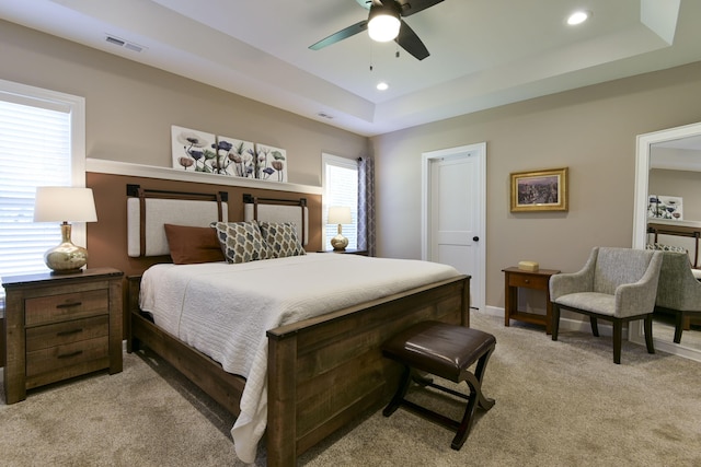 bedroom featuring ceiling fan, a raised ceiling, and light colored carpet