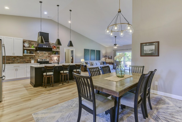 dining room with ceiling fan with notable chandelier, high vaulted ceiling, and light hardwood / wood-style flooring