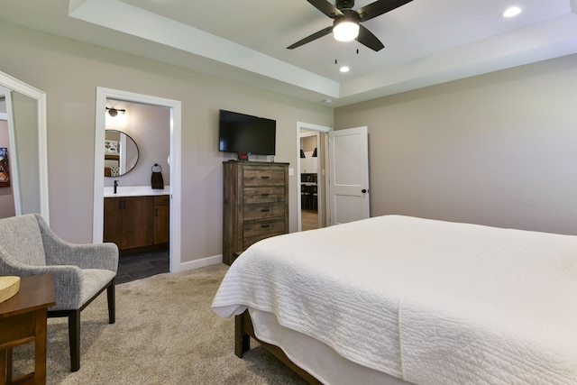 bedroom featuring ceiling fan, sink, ensuite bathroom, carpet floors, and a tray ceiling