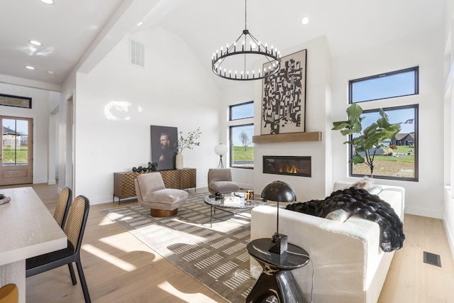 living room featuring high vaulted ceiling, a notable chandelier, light wood-type flooring, and a wealth of natural light