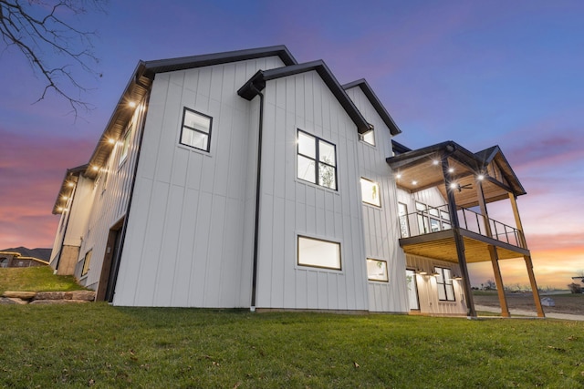 back house at dusk featuring a balcony and a yard