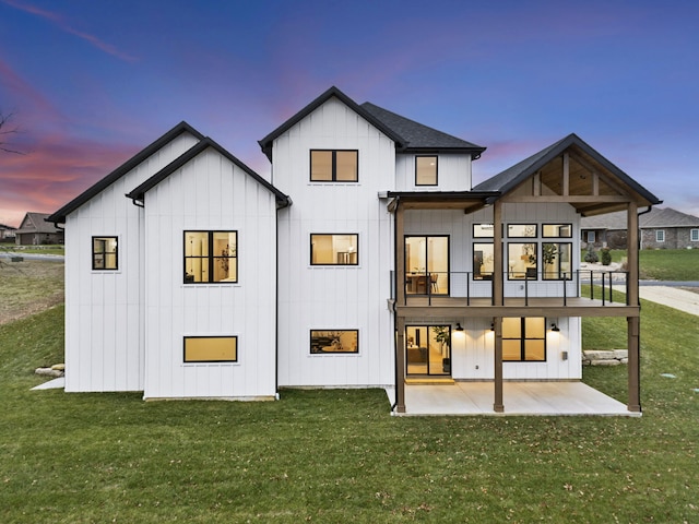 back house at dusk with a yard, a balcony, and a patio