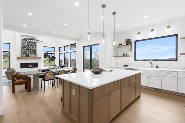 kitchen featuring a center island, sink, light stone counters, pendant lighting, and white cabinets